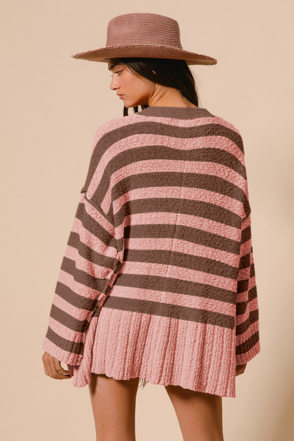 Stylish woman in a striped pink and brown cardigan with a curved hem, accessorized with a wide-brim hat. Perfect for any occasion.