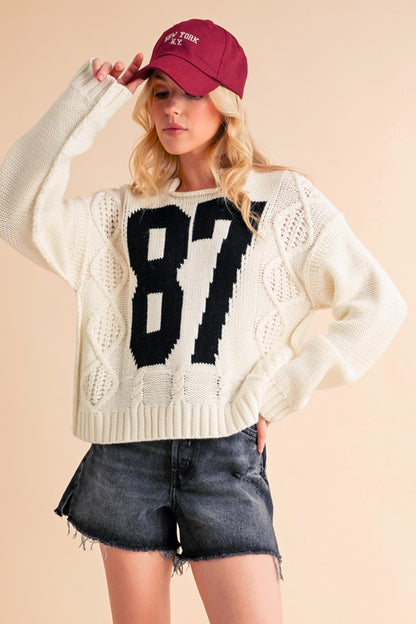 Cozy Aemi+Co cable knit drop shoulder sweater with contrasting number 87, perfect for chic Christmas style and new arrivals.