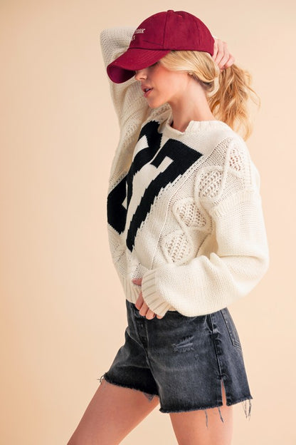 Cozy Aemi+Co contrast number cable knit sweater paired with denim shorts and a maroon cap, perfect for casual outings.